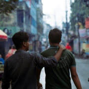 Two men walking down a busy street, with the man on the left holding the man on the right's