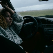 A woman sitting in a parked car with rain on the windshield.