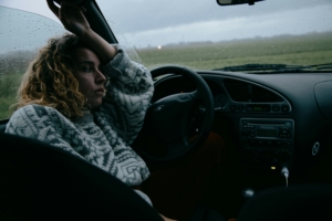 A woman sitting in a parked car with rain on the windshield.