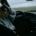 A woman sitting in a parked car with rain on the windshield.