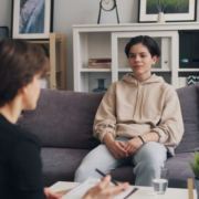A young person sitting on a couch in a therapist office, with their therapist sitting across from them.