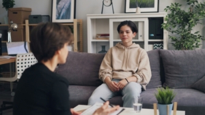 A young person sitting on a couch in a therapist office, with their therapist sitting across from them.