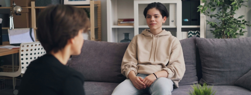 A young person sitting on a couch in a therapist office, with their therapist sitting across from them.