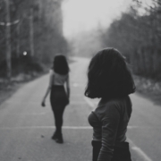 Two women with similar hair and outfits standing in the middle of a wooded road, in black and white.