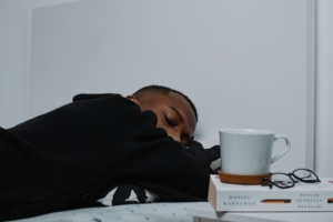 A young man asleep with a book and coffee mug next to him.