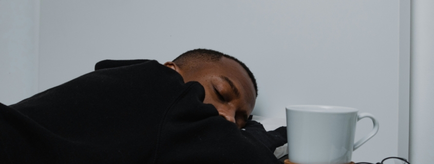 A young man asleep with a book and coffee mug next to him.