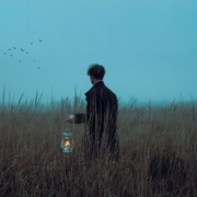 A man in a field at dawn holding a lantern.