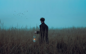 A man in a field at dawn holding a lantern.