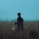 A man in a field at dawn holding a lantern.