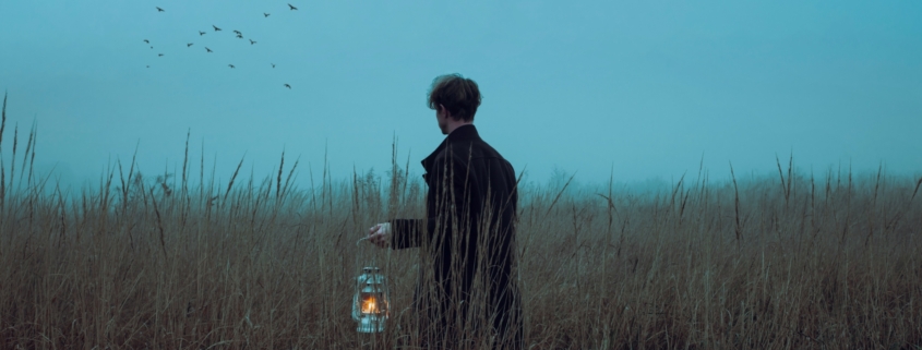 A man in a field at dawn holding a lantern.