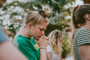 A young woman holding her hands to her chin with her head bowed and eyes closed.