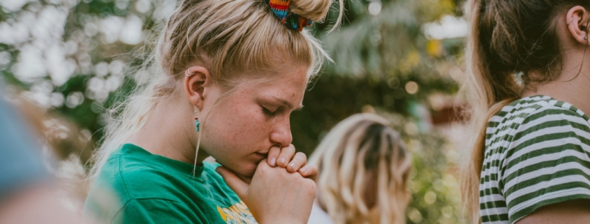 A young woman holding her hands to her chin with her head bowed and eyes closed.