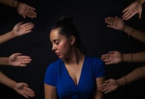 A distressed looking woman, surrounded by hands reachi