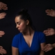 A distressed looking woman, surrounded by hands reachi