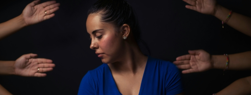 A distressed looking woman, surrounded by hands reachi