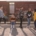A group of young people standing outside in front of a fence by a railyard.