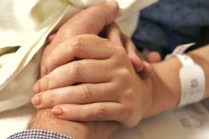 A close up of two white people holding hands. One person is wearing a hospital bracelet.