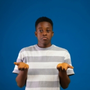 A Black teenage boy, shrugging his shoulders with his hands in the air like he's confused.