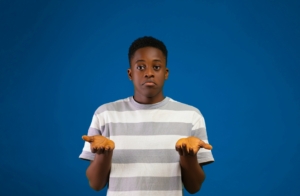 A Black teenage boy, shrugging his shoulders with his hands in the air like he's confused.