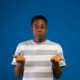 A Black teenage boy, shrugging his shoulders with his hands in the air like he's confused.