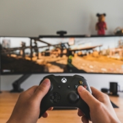 A white person's hands holding an xbox controller up in front of a monitor with a video game playing.