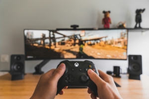 A white person's hands holding an xbox controller up in front of a monitor with a video game playing.