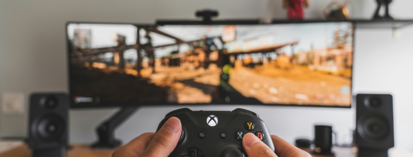 A white person's hands holding an xbox controller up in front of a monitor with a video game playing.