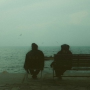 Two people sitting on a bench in front of a body of water, from behind.