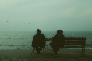 Two people sitting on a bench in front of a body of water, from behind.