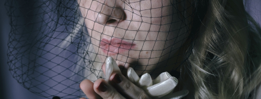 A woman with a veil on her head and her hands under her chin like she's praying.