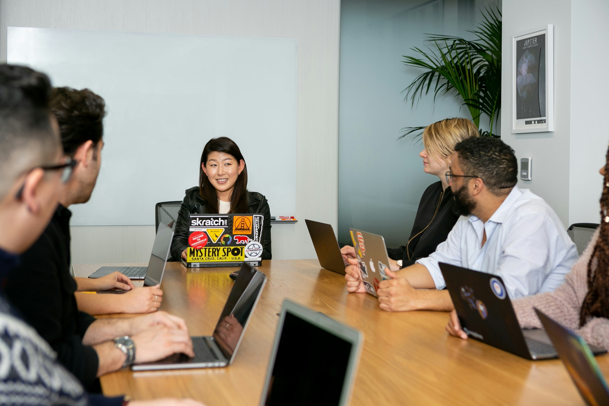 A group of people sitting at a table in a conference room, with an Asian woman sitting at the head of the table.