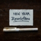 A white piece of paper with "New Year Resolutions" written on it in black pen, on a dark background.