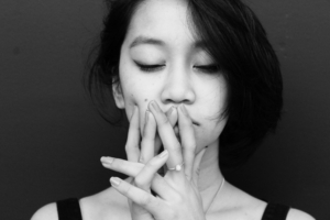 A black and white photo of an Asian woman looking sad and holding her hands up to her mouth like she's thinking.