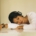 A young South Asian woman with headphones on laying her torso on a table indoors, looking distressed.