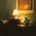 A person sleeping at a desk in a dark room in front of a lamp.