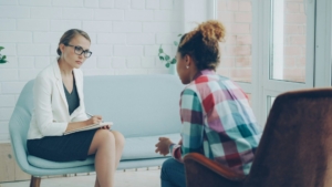 A white therapist sitting across from a Black patient in a therapy office.