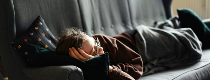 Woman in sweats laying on a gray couch