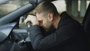 White man resting his head on the steering wheel of car