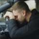White man resting his head on the steering wheel of car