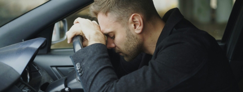 White man resting his head on the steering wheel of car